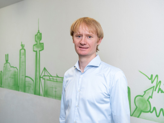 Dr._Alex_Greilich.jpg Portraitfoto von Dr. Alex Greilich vor einer weißen Wand mit grüner Dortmunder Graffiti-Skyline