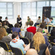 Podiumsdiskussion Im Vordergrund sind Zuhörer einer Podiumsdiskussion zu sehen. Im Hintergrund sind die Referenten zu erkennen.