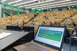 Ein aufgeklappter Laptop steht auf einem Pult in einem Hörsaal.