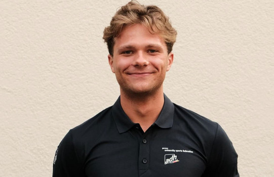 Porträtfoto Noel Jaschke: Das Foto zeigt Noel Jascke in einem schwarzen Poloshirt. Jaschke hat blonde Haare und lächelt in die Kamera.