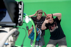 Zwei junge Menschen posieren vor einem Green Screen in eine Filmkamera.