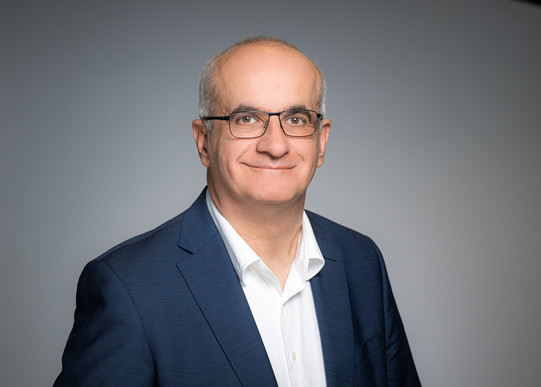 Porträtfoto von Prof. Manfred Bayer: Prof. Bayer trägt einen Anzug und eine Brille und steht vor einem grauen Hintergrund. Er lächelt in die Kamera.