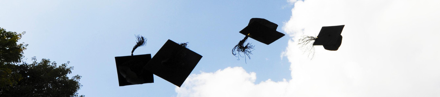 Four black doctoral caps thrown into the air
