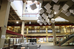 Ein leeres Foyer in einem Gebäude. Links im Vordergrund stehen Stühle und Tische. Im Hintergrund leere Bücherregale. Darüber leere Flure und Treppen.