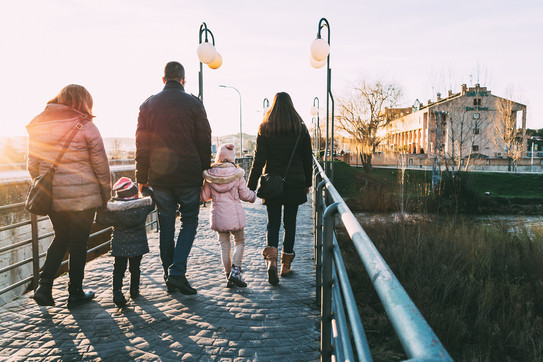 Das Foto zeigt eine Familie beim Spazierengehen. Zwei Kinder werden von drei Erwachsenen, einem Mann und zwei Frauen, an den Händen gehalten.