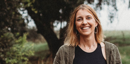Porträtfoto von Prof. Julia K. Vogel: Ein körniges Bild, das Prof. Julia K. Vogel in der Natur zeigt. Sie hat blonde Haare. Im Hintergrund steht ein Baum auf einer Wiese.