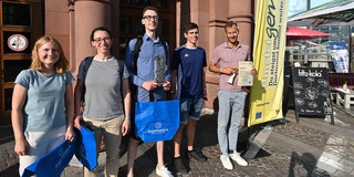 Zwei junge Frauen und drei junge Männer stehen mit Preisen vor dem Eingang einer Veranstaltungshalle.