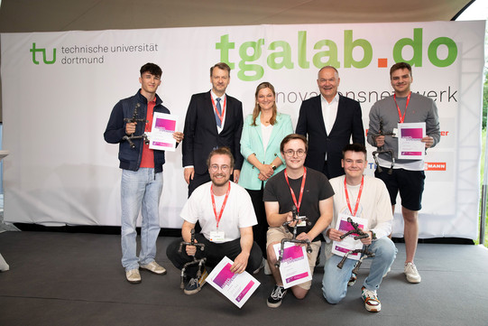 Eine Gruppe von Personen. Mehrere Studenten halten eine Urkunde in der Hand.