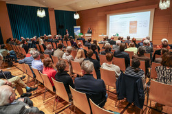 Das Bild zeigt den Saal mit Publikum aus einem hinteren Eckwinkel. Hinterm Rednerpult steht Prof. Aladin El-Mafaalani, neben ihm hängt eine große Leinwand, auf der eine Präsentation zu sehen ist.