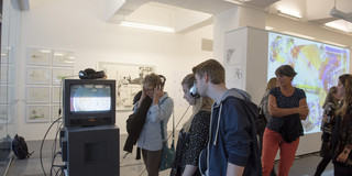 Visitors to the art tour watch the film of an exhibit and listen via headphones 