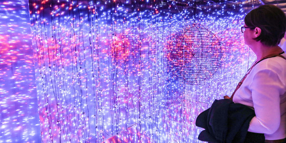 Eine Frau steht vor einer Installation aus Draht-Kugeln und blauen und pinken Lichterketten
