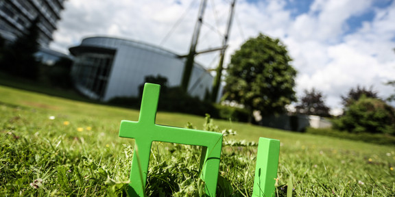 TU-Logo auf dem Rasen. Im Hintergrund das Audimax.