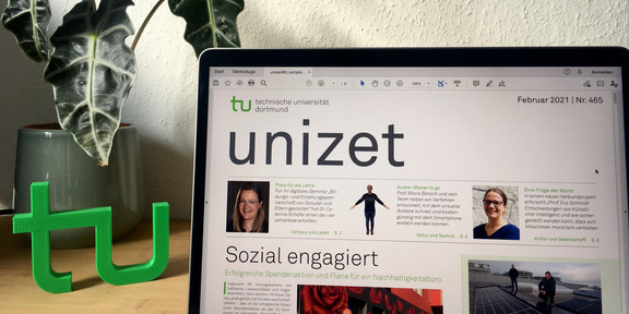 [Translate to English:] Laptop mit einer Ausgabe der unizet, einem TU-Logo und einer Pflanze auf einem Schreibtisch