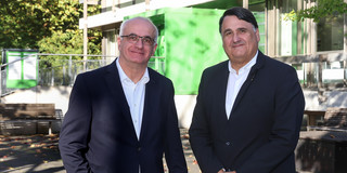 Foto: Prof. Manfred Bayer, Rektor der TU Dortmund, und Prof. Martin Paul, Rektor der Ruhr-Universität Bochum, stehen vor einem grünen Gebäude und lächeln in die Kamera.