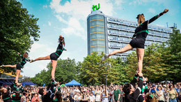 Zu sehen ist der Auftritt einer Cheerleader-Gruppe. Drei Chearleaderinnen werden von je drei Personen in die Luft gehoben. Im Hintergrund stehen viele Menschen.