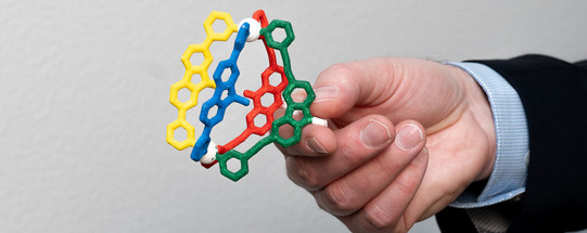 Eine Hand hält einen bunten 3D-Druck einer Molekülstruktur. 