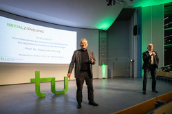 Prof. Dr. Klaus von Klitzing und Prof. Manfred Bayer auf einer Bühne. Im Hintergrund das TU-Logo und eine Präsentation mit der Überschrift "Initialzündung"