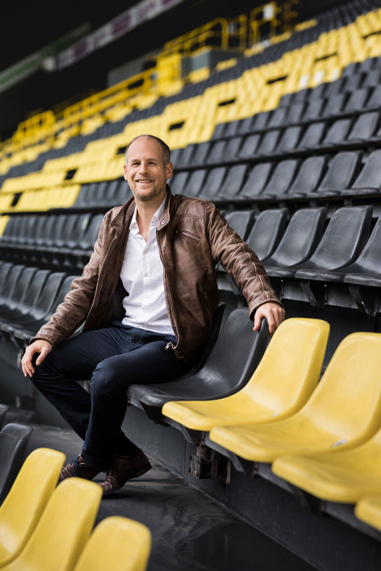 Foto: Ein Mann in brauner Lederjacke sitzt auf den gelb-schwarzen Rängen des BVB-Stadions in Dortmund.