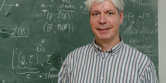 A man stands in front of a blackboard with mathematical formulas