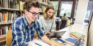 Lernen in der Bibliothek Zwei Studierende sitzen mit Lernmaterialien an einem Tisch in einer Bibliothek.