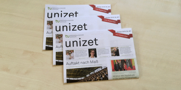 Drei Ausgaben der unizet liegen übereinander auf einem Tisch.