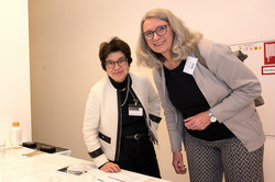 Das Bild zeigt zwei erwachsene Frauen, die hinter einem Tisch stehen und in die Kamera lächeln.