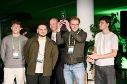 Foto: Fünf Personen stehen zusammen, während eine Person eine Auszeichnung hochhält und eine andere applaudiert.