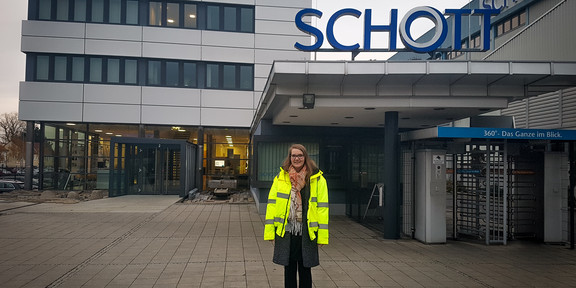 Rabea Friedrich Eine junge Frau in Warnjacke steht vor einem mehrstöckigen Gebäude der Firma SCHOTT