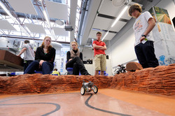Personen beobachten ein Miniaturmodell der Marsmission. 