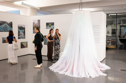 Ein Teil der Ausstellung. Neben einer weißen Wand mit Fotos hängt ein weißes Netz von der Decke. 
