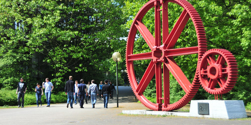 Kunstinstallation eines großen, rot lackierten Industriezahnrads auf dem Campus Nord