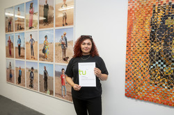 Rundgang Kunst Kunstpreis Fotografie Eine Studentin mit Urkunde steht zwischen 15 Fotoportraits links und einer verwebten Fotoarbeit rechts.