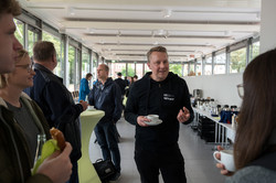Bei einem Empfang stehen Menschen in einer lockeren Runde zusammen und tauschen sich aus. Manche von ihnen haben ein Getränk oder einen Snack in der Hand.
