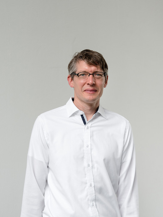 Portraitbild eines Mannes, der eine Brille und ein weißes Hemd trägt.