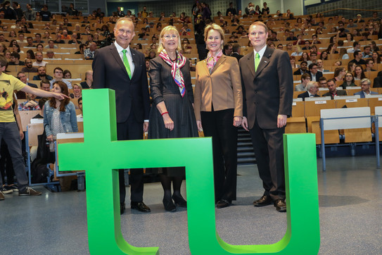 Frances Arnold Gruppenfoto Audimax Im Vordergrund steht das TU-Logo, im Hintergrund stehen Andrzej Górak, Ursula Gather, Frances Arnold und Stephan Lütz