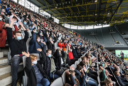 Oktober Erstsemesterstudierende, die auf einer Tribüne in einem Fußballstadion mit Mund-Nasen-Bedeckung sitzen, reißen ihre beiden Arme hoch und machen eine La-Ola-Welle.