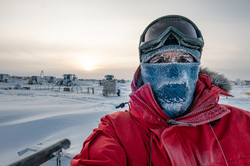 Selfie of man in red jacket standing outside in snow with scarf, eyelashes and eyebrows covered with ice