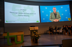 Eine Videobotschaft, in der Thomas Westphal zu sehen ist, wird an die Wand des Audimax der TU Dortmund projiziert.