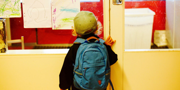 Ein Kind mit blauem Schulranzen steht vor der Tür eines Klassenzimmers.