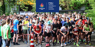 Läufer*innen an der Startlinie des Campuslaufs kurz vor dem Startschuss, oben ist das Logo der FISU-Games ins Bild montiert