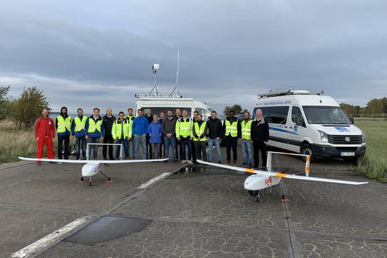 Forschungsprojekt LARUS Eine Gruppe von Menschen steht hinter zwei unbemannten Starrflügelflugzeugen.