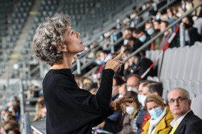 Eine Frau steht vor einer Tribüne in einem Fußballstadion und übersetzt die Erstsemester-Begrüßung der TU Dortmund für alle Zuschauer*innen auf der Tribüne in Gebärdensprache.