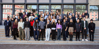 The picture shows a group photo of many different people, which was taken outside on a staircase in front of a building.