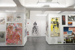 Mehrere Bilder einer Kunstausstellung hängen an einer weißen Wand.