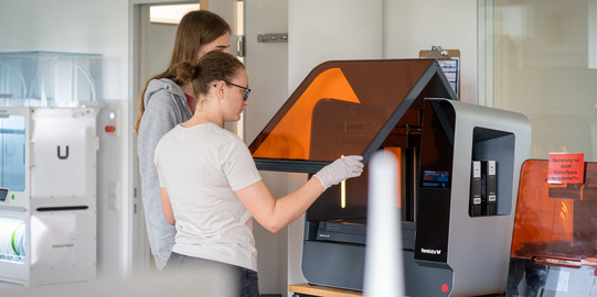 Zwei Personen in einem Labor bedienen gemeinsam einen Formlabs 3D-Drucker. 