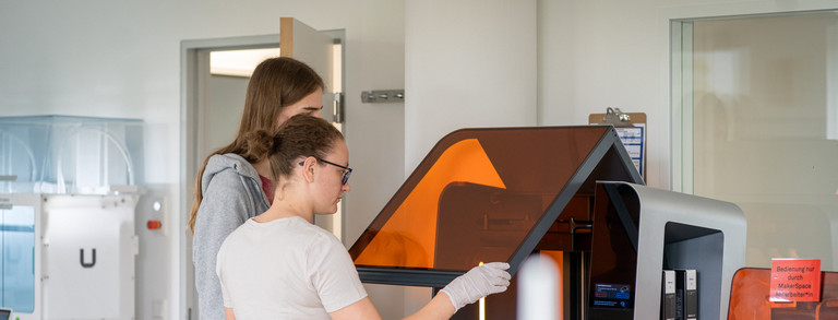 Zwei Personen in einem Labor bedienen gemeinsam einen Formlabs 3D-Drucker. 