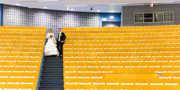 Melanie Schmidt und ihr Mann im Audimax, sie trägt ein Hochzeitskleid, er einen Anzug. 