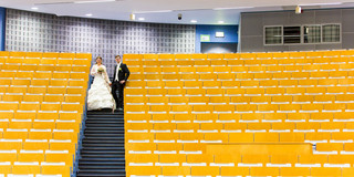 Schmidt Melanie Schmidt und ihr Mann im Audimax, sie trägt ein Hochzeitskleid, er einen Anzug.