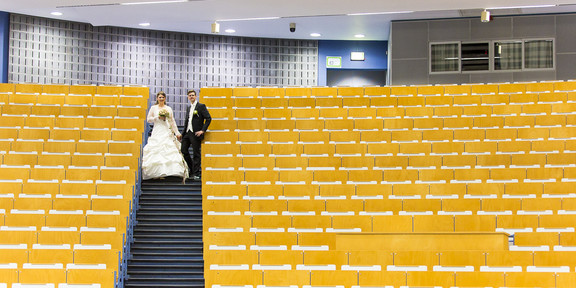 Melanie Schmidt und ihr Mann im Audimax, sie trägt ein Hochzeitskleid, er einen Anzug. 