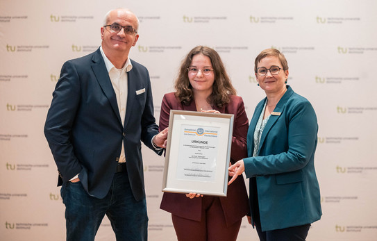 Zu sehen ist die Soroptimist-Preisträgerin Judith Bose mit ihrer Urkunde in der Hand mit dem Rektor auf der linken Seite und der Präsidentin des Soroptimist International Clubs Dortmund Daniela Fischer auf der rechten Seite.